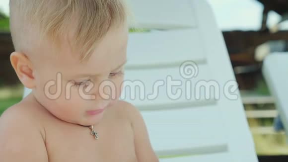 一个一岁的男孩吃饼干在海滩上的白色日光浴床上和一个小孩子在海上休息视频的预览图