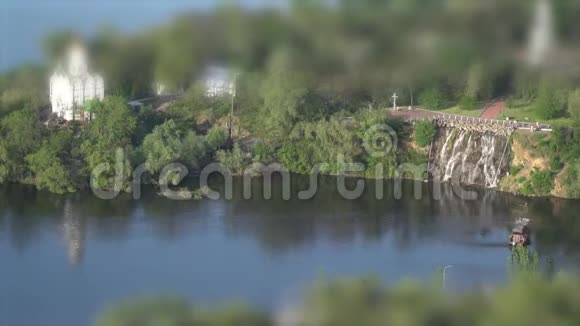 拍摄倾斜移位一座小岛上有瀑布和一座教堂沿河漂浮的木船视频的预览图