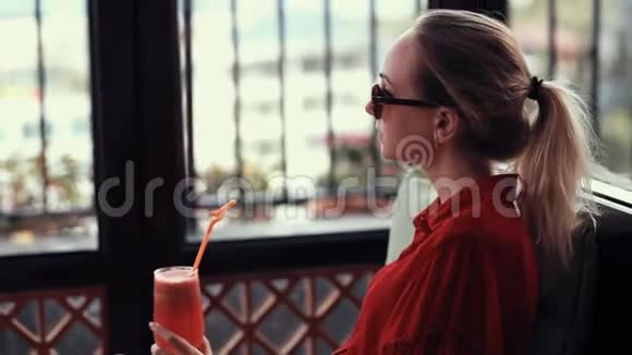 一个穿着红色裙子的年轻女孩正在酒店大厅喝一杯红色鸡尾酒戴眼镜的女孩头发聚集在视频的预览图
