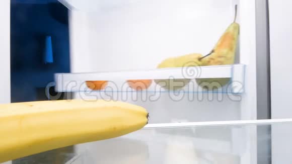 4K镜头年轻微笑的女人从冰箱里拿香蕉剥皮咬香蕉视频的预览图