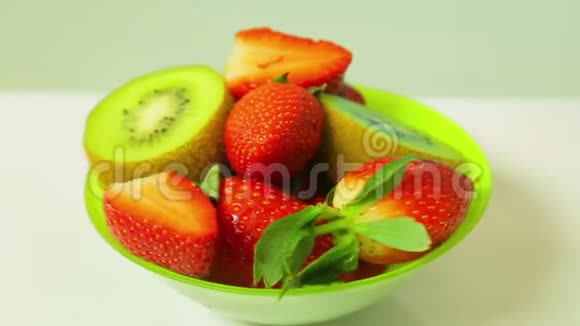 鲜奇异果和切片草莓在蓝色背景上的绿色盘子旋转成一个圆圈从上面看视频的预览图
