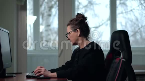 戴眼镜的成熟黑发女人坐在椅子上在办公室里用电脑工作视频的预览图