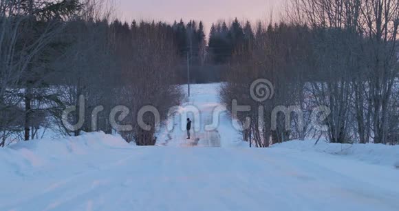 孤独的人站在夕阳下荒芜的冬日道路上视频的预览图
