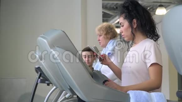 漂亮的黑发女人在跑步机上用电话走路视频的预览图