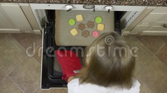 顶部的年轻的白人金发女孩推托盘与姜饼干在家厨房烤箱高角度顶部视频的预览图