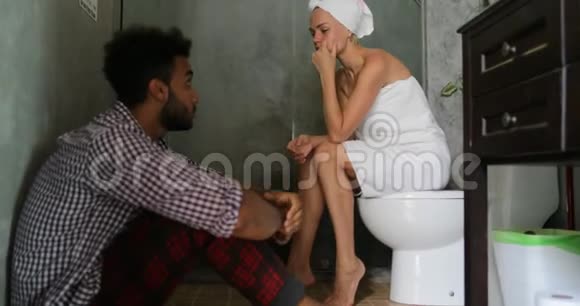 年轻夫妇在浴室里不开心男人和女人争论有问题女孩哭着坐在地板上的马桶上视频的预览图