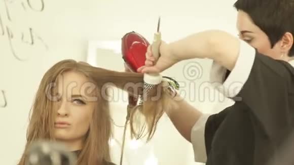 美丽的女人在美容院用吹风机和梳子给长发发型把剪发器烘干的女人视频的预览图