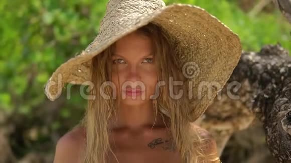 美丽的金发异国女人戴着纹身的夏帽在海滩上休息她举止端庄看着镜头视频的预览图