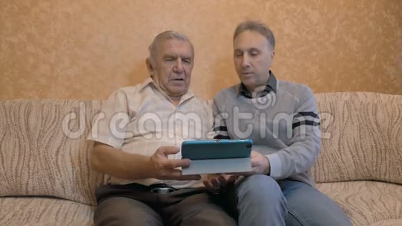 老人和他成年的儿子看看平板电脑儿子教父亲使用现代技术视频的预览图