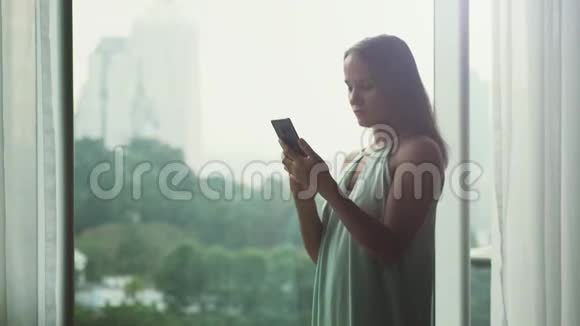 年轻漂亮的女商人用手机站在全景窗口与城市的视野3840x2160视频的预览图
