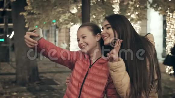 妈妈和女儿晚上在城市街道上的智能手机上自拍视频的预览图