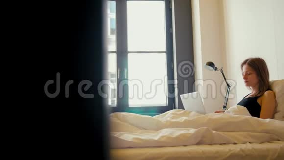 早晨女人躺在床上躺在舒适的公寓里家里有笔记本电脑视频的预览图