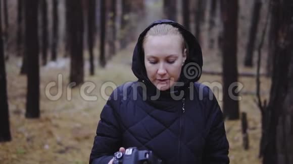 一位专业摄影师手里拿着相机穿过森林看着她拍的照片视频的预览图