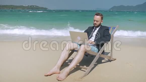年轻的商人正在热带海滩上工作他的笔记本电脑视频的预览图