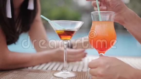一对年轻夫妇在泳池边喝鸡尾酒的特写镜头视频的预览图
