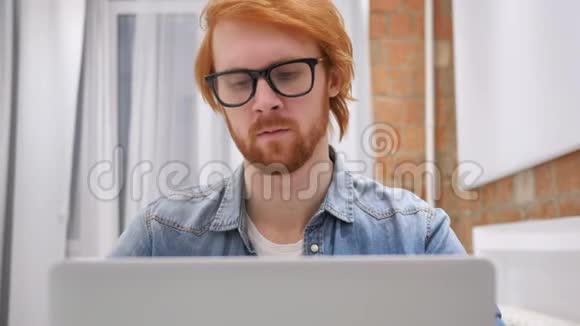 累了的红发胡子男在笔记本电脑上工作努力放松视频的预览图