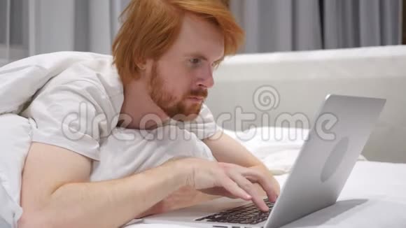 头痛红色胡子人在床上用笔记本电脑视频的预览图