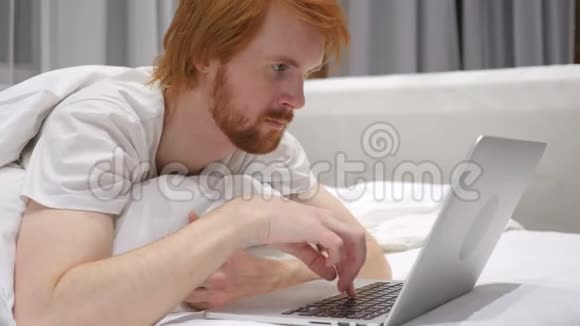 快乐的红头发胡子男床上反应工作成功视频的预览图