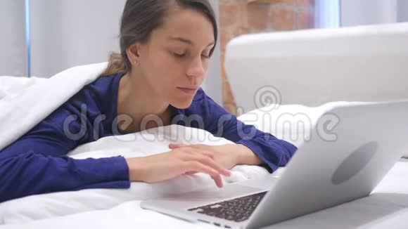 头痛迟钝的西班牙妇女在床上的笔记本电脑上工作工作量视频的预览图