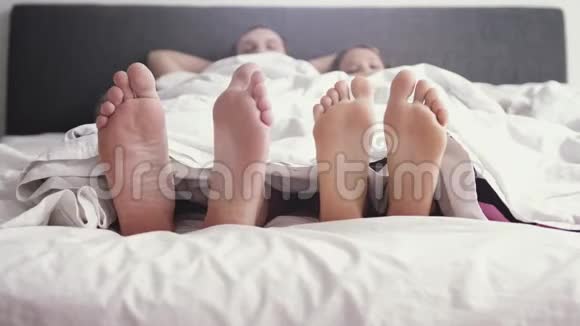 年轻可爱的快乐夫妇在毯子下玩耍和跳舞而早上醒来在床上慢动作视频的预览图