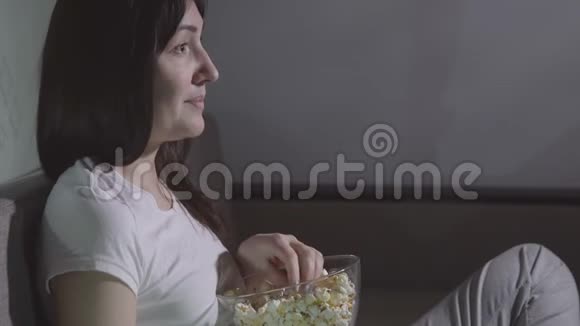 晚上一个年轻的女人独自用爆米花看电影视频的预览图