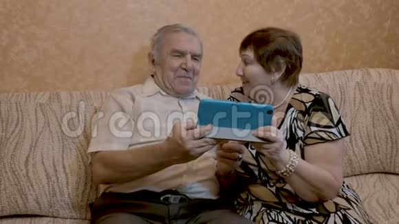 一对成年夫妇使用平板电脑他们坐在沙发上视频的预览图