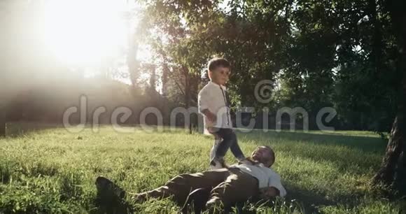 年轻的父亲和他的小儿子正在后院玩耍他们躺在草坪上太阳落山了视频的预览图
