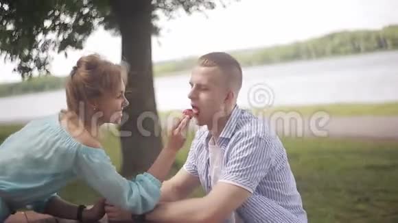 在河边约会的快乐情人女孩给男朋友喂草莓视频的预览图