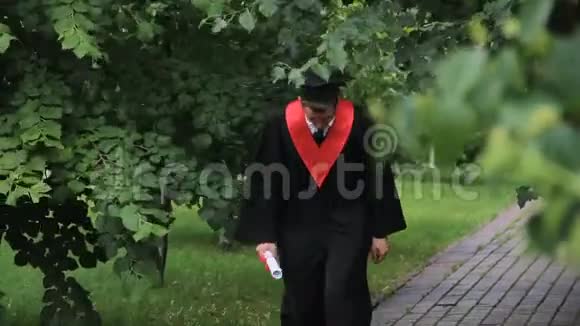 穿着学术服装拿着文凭在公园里散步和跳跃的人很高兴视频的预览图