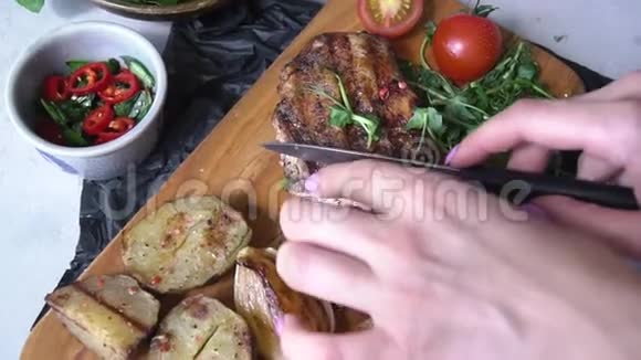 一个女人用蔬菜和木盘切肉饼旁边有炸土豆和新鲜蔬菜视频的预览图