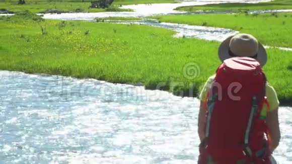 那个带着红色背包的旅行者女人坐在河岸上山区视频的预览图