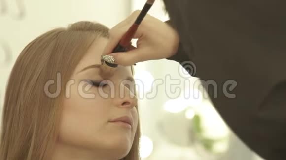 化妆师在美容工作室使用化妆刷来化妆眼睛为年轻的女人做化妆视频的预览图