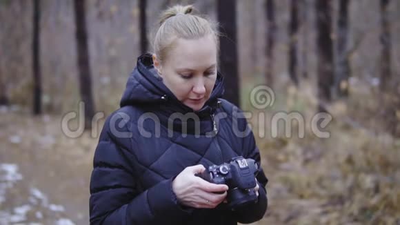 手里拿着相机的女孩摄影师翻看拍摄的照片秋天的森林第一场雪电影视频的预览图