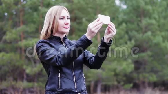 女孩在树林里用电话拍照视频的预览图