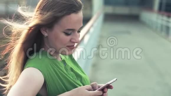 城里一个年轻女孩带着一部智能手机读留言绿色连衣裙视频的预览图