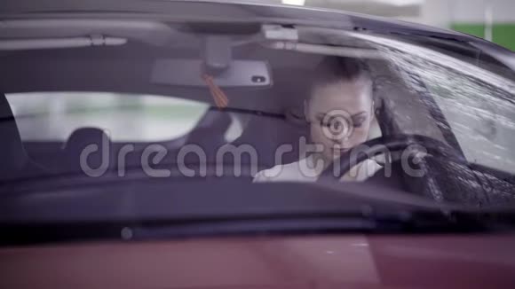 漂亮的女性穿着白色衬衫坐在方向盘后面的红色汽车上视频的预览图