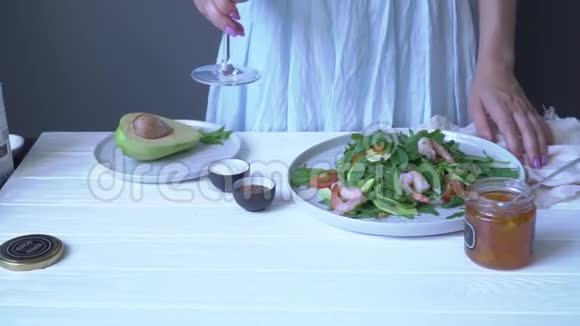 一个女人在一张桌子上放着沙拉盘子里放着一罐酱汁和鳄梨盛满了一杯白葡萄酒视频的预览图