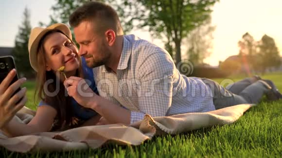 一对相爱的情侣躺在公园的格子布上在日落时分合影留念视频的预览图
