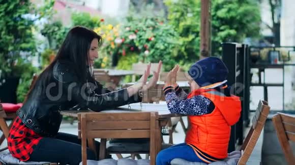 快乐的母亲和她的小儿子在城市咖啡馆里玩耍和欢笑视频的预览图