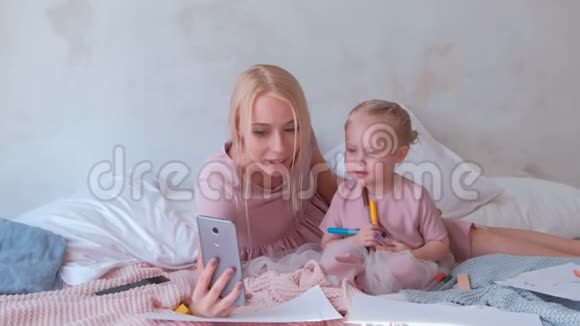 年轻迷人的金发妈妈和她穿着粉红色连衣裙的小迷人女儿在手机上拍照视频的预览图