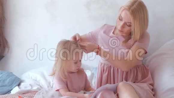 年轻迷人的金发母亲把头发扎成辫子她的小女儿穿着粉红色的连衣裙而她画的是视频的预览图