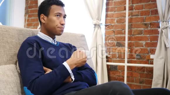 年轻的非洲男人喝杯咖啡坐沙发视频的预览图
