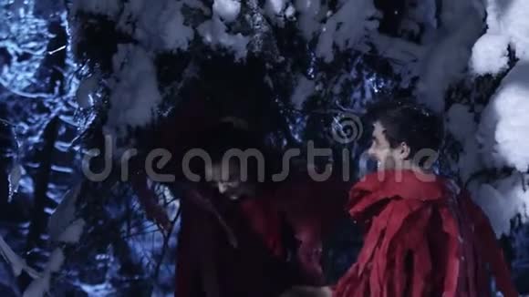 可爱的男人和女人在寒冷的夜晚在白雪皑皑的冬木中慢慢移动视频的预览图