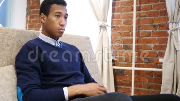脖子受伤疲惫的非洲青年坐在沙发上视频的预览图
