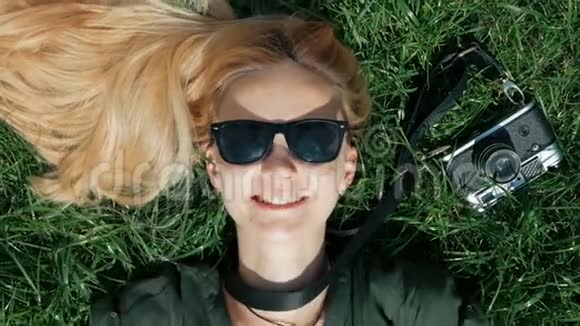 美丽的金发女孩躺在草地上到处都是傻瓜起飞戴上一顶躺在草地上的帽子概念视频的预览图