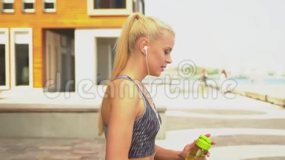 年轻迷人和运动的金发女孩穿着运动服装听音乐和放松的户外保健体育视频的预览图