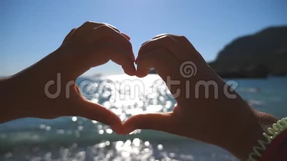 在阳光明媚的一天年轻女孩用双手在海洋背景上做心形海滩上的暑假概念视频的预览图