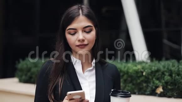 职业年轻女商人用智能手机在城市街道上散步喝咖啡她看着摄像机视频的预览图