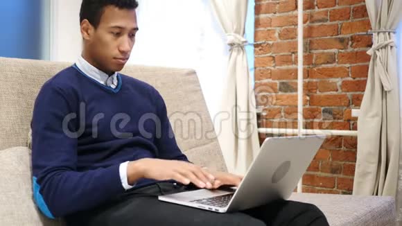 非洲男人在笔记本电脑上做视频聊天坐在沙发上视频的预览图