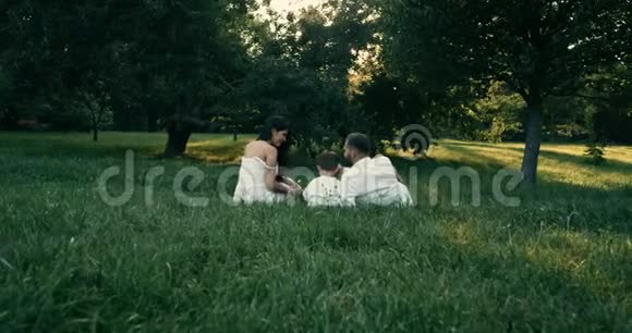 微笑的家人互相拥抱同时坐在绿色的田野上4k视频的预览图